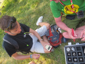 显示两个年轻人的图象，坐在Glastonbury音乐节的一片草地上。他们拿着来自Cirrus Research的DoseBadge噪声剂量计